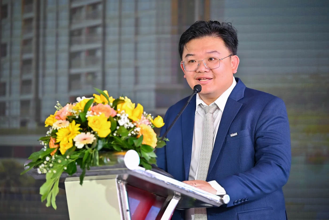 Đại diện chủ đầu tư phát biểu trên bục tại lễ khởi công, phía trước có bình hoa