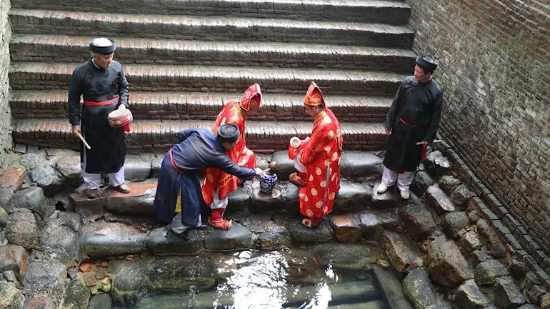 Bốn người mặc trang phục Quan họ bên bậc đá dẫn xuống giếng Ngọc ở làng Diềm